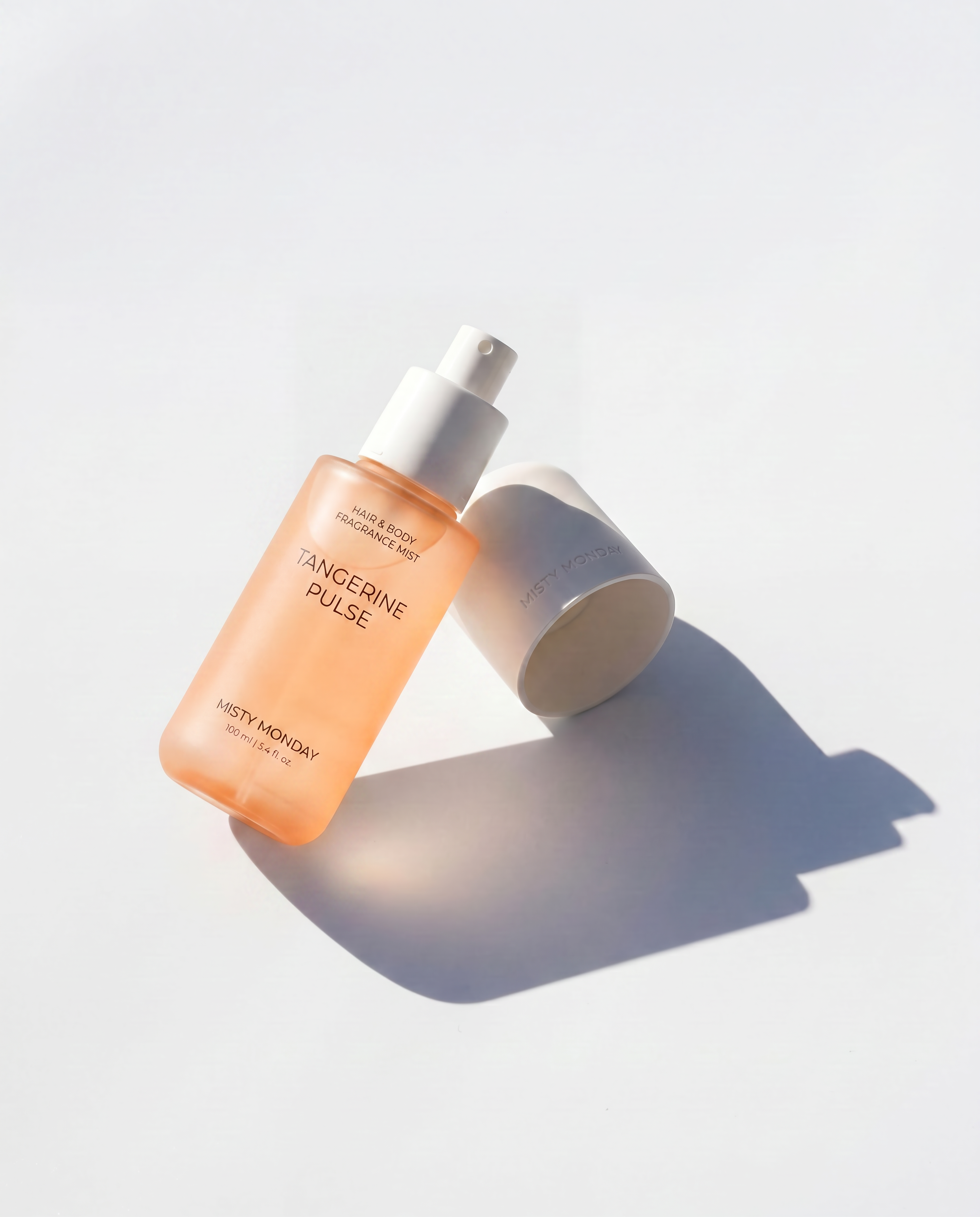 Misty Monday Tangerine Pulse haj és testpermet fehér felületen kupakra fektetve, árnyékkal